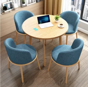 Round light wood-look table with four blue upholstered chairs and a laptop by a window