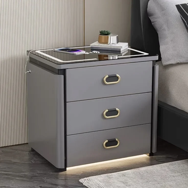 Gray three-drawer nightstand beside a bed with a phone charging on the glass top and a light strip under the base