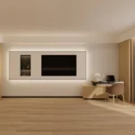 TV wall with a lit display niche beside a light-wood desk with an upholstered chair