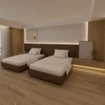 Twin beds with brown upholstered bases in front of the padded headboard wall, seen from the foot of the beds