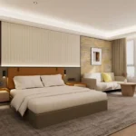 King room with an olive upholstered bed, tan padded headboard, vertical-channel wall panel, cream sofa and round wood table