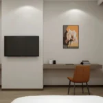 Wall-mounted TV above a long taupe wall-hung desk with a rust-colored chair and a framed picture
