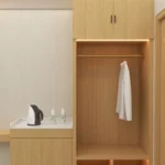 Open wardrobe with hanging rail, two-door cabinet above and lit shoe cubbies, beside a counter with a kettle