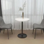 Round table with a white stone-look top and black base, with two gray upholstered chairs in front of a window