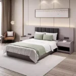 Bed with a charcoal padded headboard on a gray backboard, an open-shelf bedside table and an armchair, with a green throw