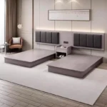 Two gray wood-grain platform bed bases side by side with charcoal padded headboards and a bedside table with slippers