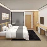 Room view with twin beds on a black rug, a long desk with white cabinet doors, a wall-mounted TV and a tall cabinet