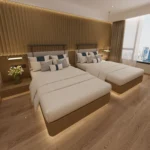 Twin beds with warm-wood bases and padded headboards seen from the side, with the window behind