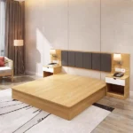 Light-oak platform bed with a dark gray padded headboard in vertical strips, black wall lights and white-drawer nightstands