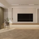 Wall-mounted TV above a long wall-hung ledge with a gray chair, on a light herringbone floor