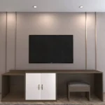 Wall-mounted TV above a long dark walnut desk with a white two-door cabinet and a gray stool