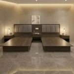 Two dark walnut platform bed bases with padded headboards and three nightstands with table lamps, on a stone floor