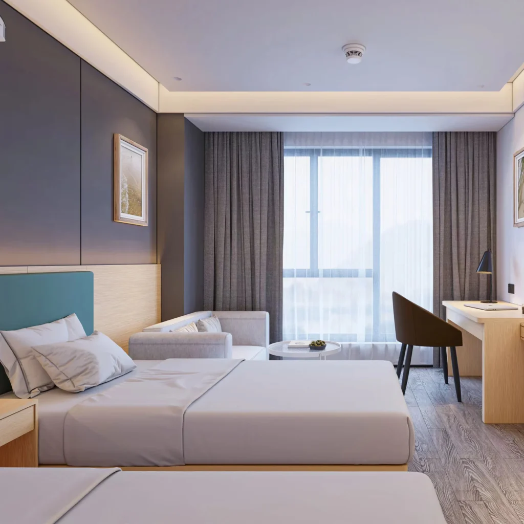 Bed with a teal-blue padded headboard on a light-wood wall panel, a gray sofa with a round table and a desk with chair