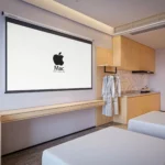 Pull-down screen above a long light-wood ledge, a hanging rail with robes and kitchenette cabinets on the right