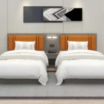 Twin beds with orange padded headboards on a gray backboard, a shared nightstand with a reading light and a phone