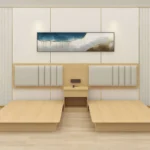 Twin light-wood bed bases with beige padded headboards in vertical strips and a small nightstand with sockets between