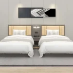 Twin beds with cream-yellow padded headboards on a gray backboard with a shared nightstand