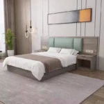 Made-up bed with a mint-green padded headboard, brown runner and two nightstands, with a plant and pendant lights