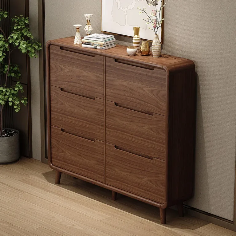 Walnut-tone shoe cabinet with six groove-handle fronts in two columns, rounded corners and slim legs, beside a wall