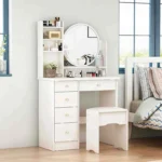 White vanity desk with a round mirror, open shelves, four stacked drawers and a stool, beside a bed