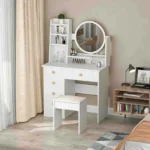 White vanity desk with a round mirror, open shelves and a stool, beside a desk lamp and a bookshelf