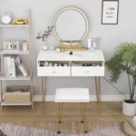 White vanity with both drawers pulled open and a round mirror on a gold-tone base, with a padded stool