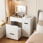 White foldaway vanity with a lit flip-up mirror and the seat pulled out, beside a bed