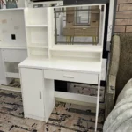 White vanity desk with a rectangular mirror, open shelves, a door cabinet and a drawer, in front of a patterned rug