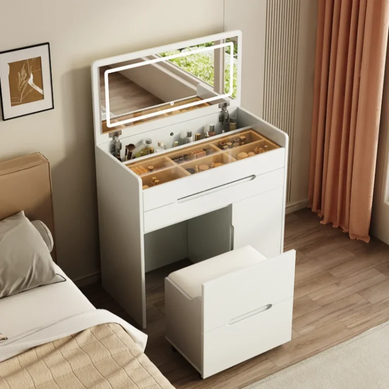 Cream-white flip-top vanity with the lid up, a lit LED mirror, a divided tray and a pull-out seat, beside a bed