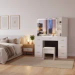 White vanity with a lit LED mirror, seven drawers and a stool, beside a bed and a bedside table