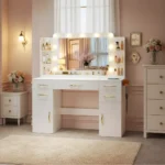 White vanity with a bulb-lit mirror, open shelves, gold-tone curved pulls and door cabinets, in a pink room