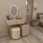 Blush-pink vanity with an LED-ring mirror, the side unit and a cream stool, beside a bed