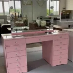 Pink Hollywood vanity with a bulb mirror, a glass-covered top, a wide center drawer and drawer banks, in a showroom
