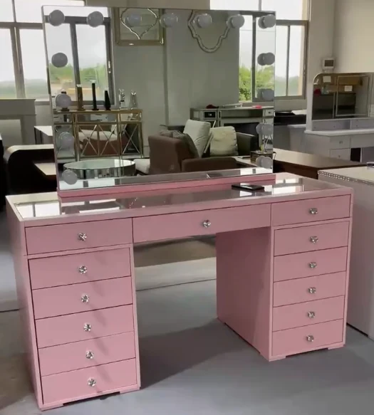 Pink Hollywood vanity with a bulb mirror, a glass-covered top, a wide center drawer and drawer banks, in a showroom