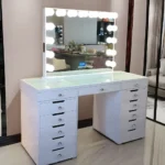 White vanity with a lit bulb mirror, a glass-covered top and two drawer banks, on a marble-look floor