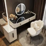 Cream vanity with a black glass top, a black-framed round LED mirror and a cream scalloped chair