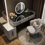 Gray vanity with a black glass top, a black-framed round LED mirror and a gray scalloped chair
