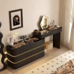 Black cabinet with gold-tone lines and a lower desk with a lit cloud-shaped mirror, beside a framed art poster and a window